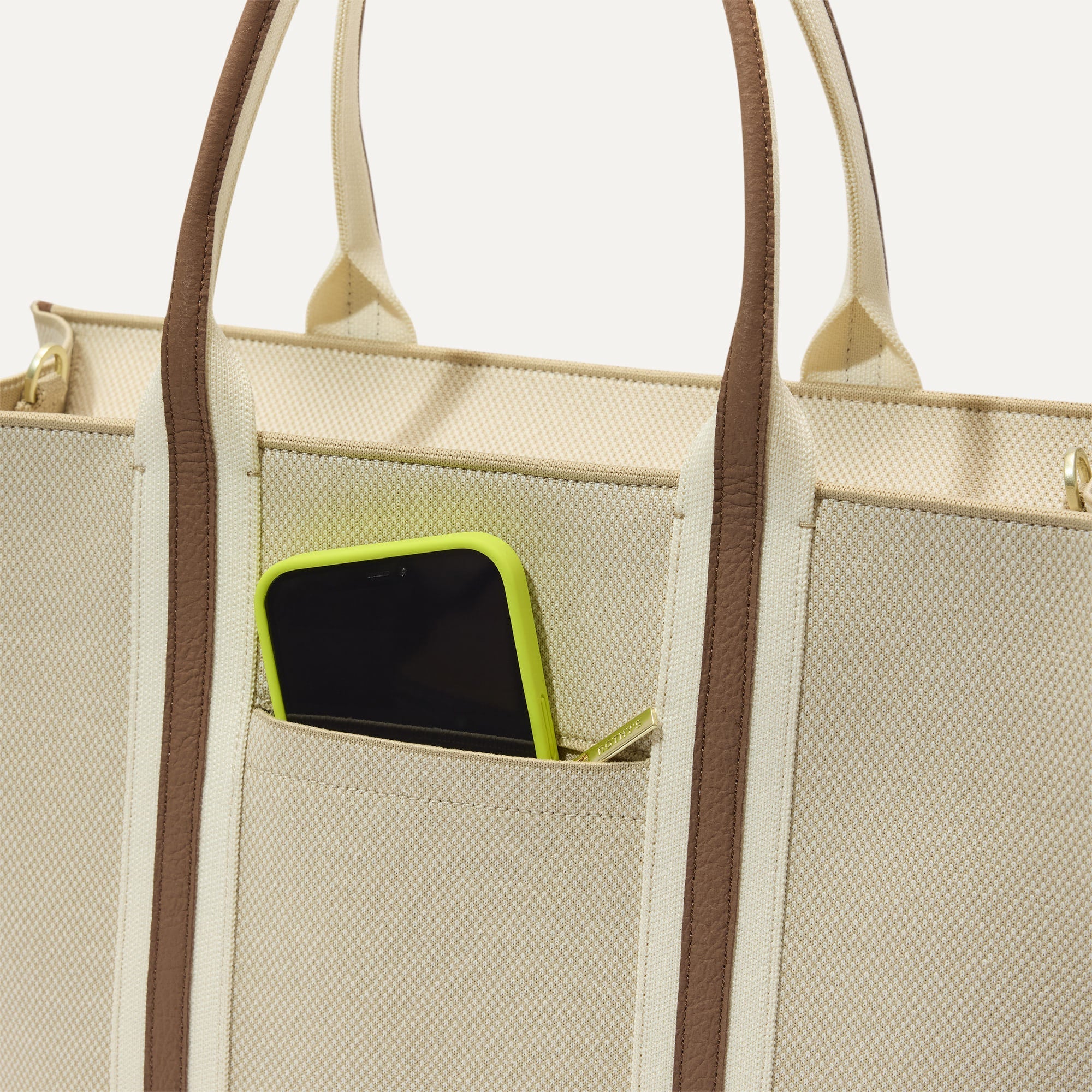 A closeup of The Classic Tote in Buttercream, focusing on the exterior zip pocket.