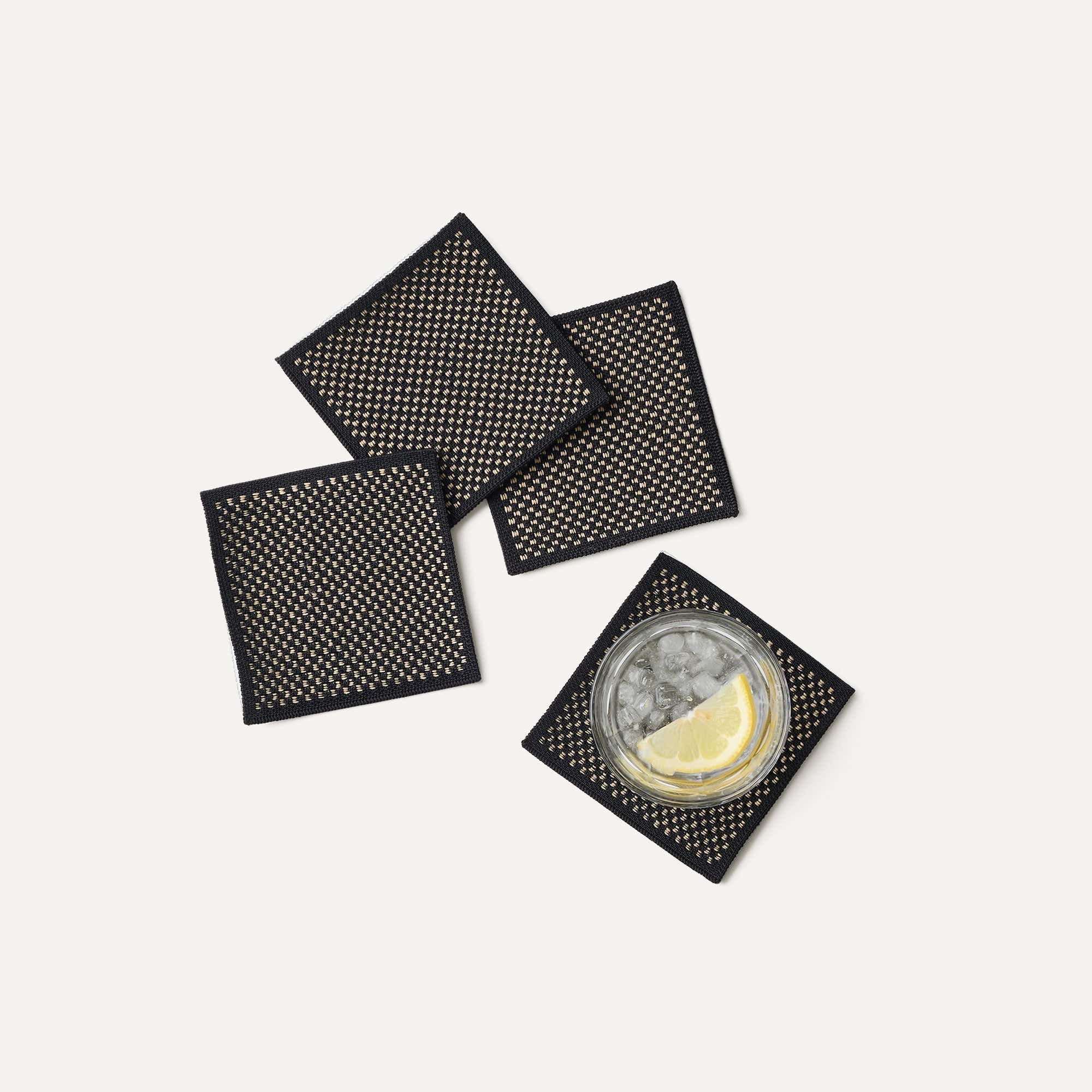 A set of four Coasters in Peppercorn shown with a drink.