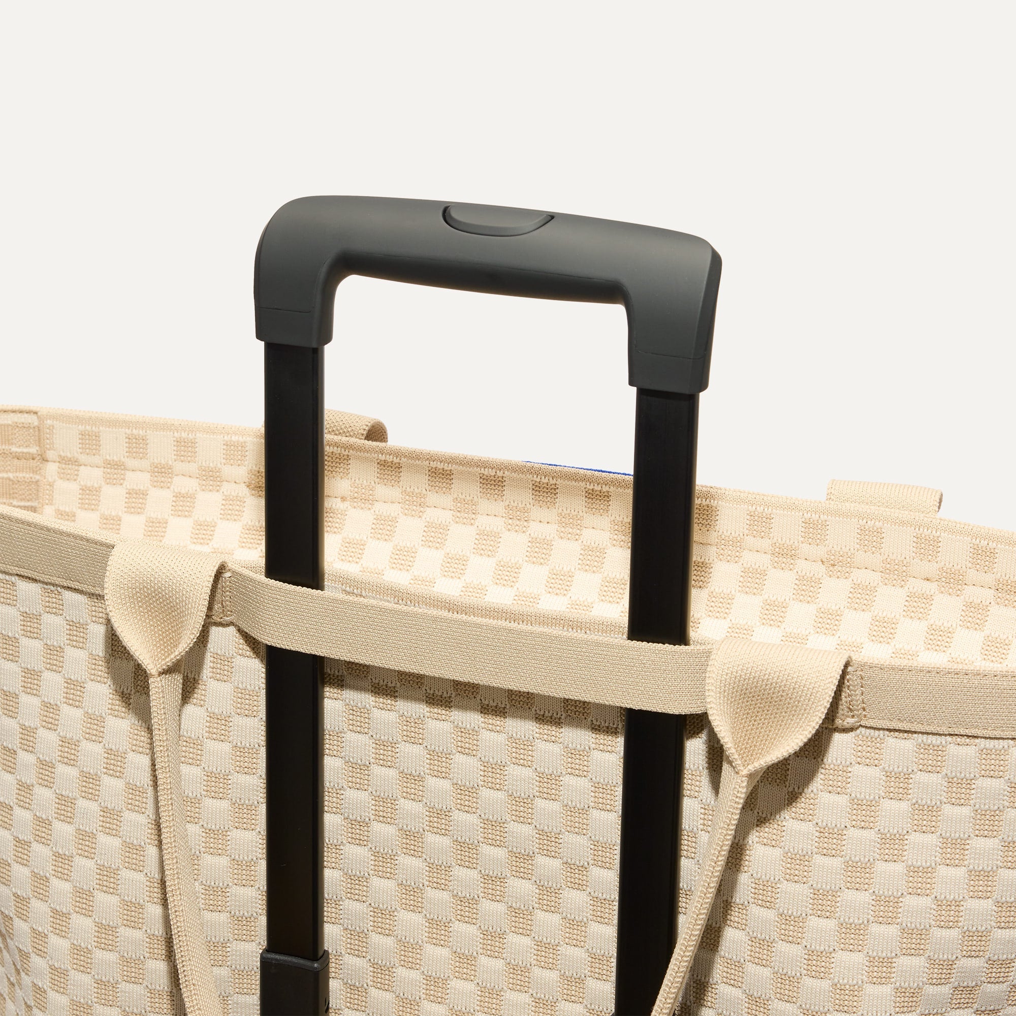 The Zip Travel Tote in  Parchment Basketweave, shown attached to a rolling suitcase using the wrap-around band.