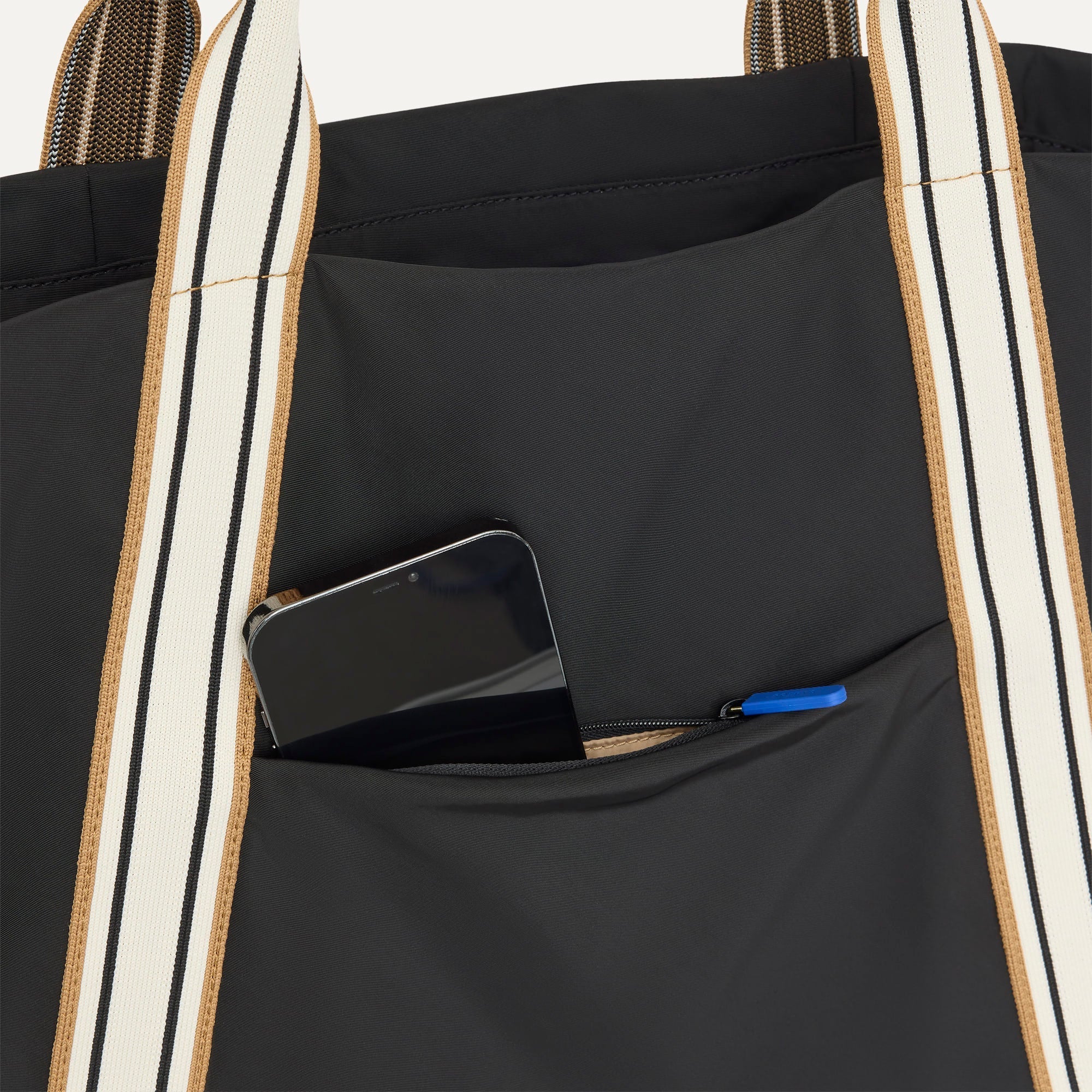 A close up of The Travel Tote in Ink with a phone slipped into the outer pocket.