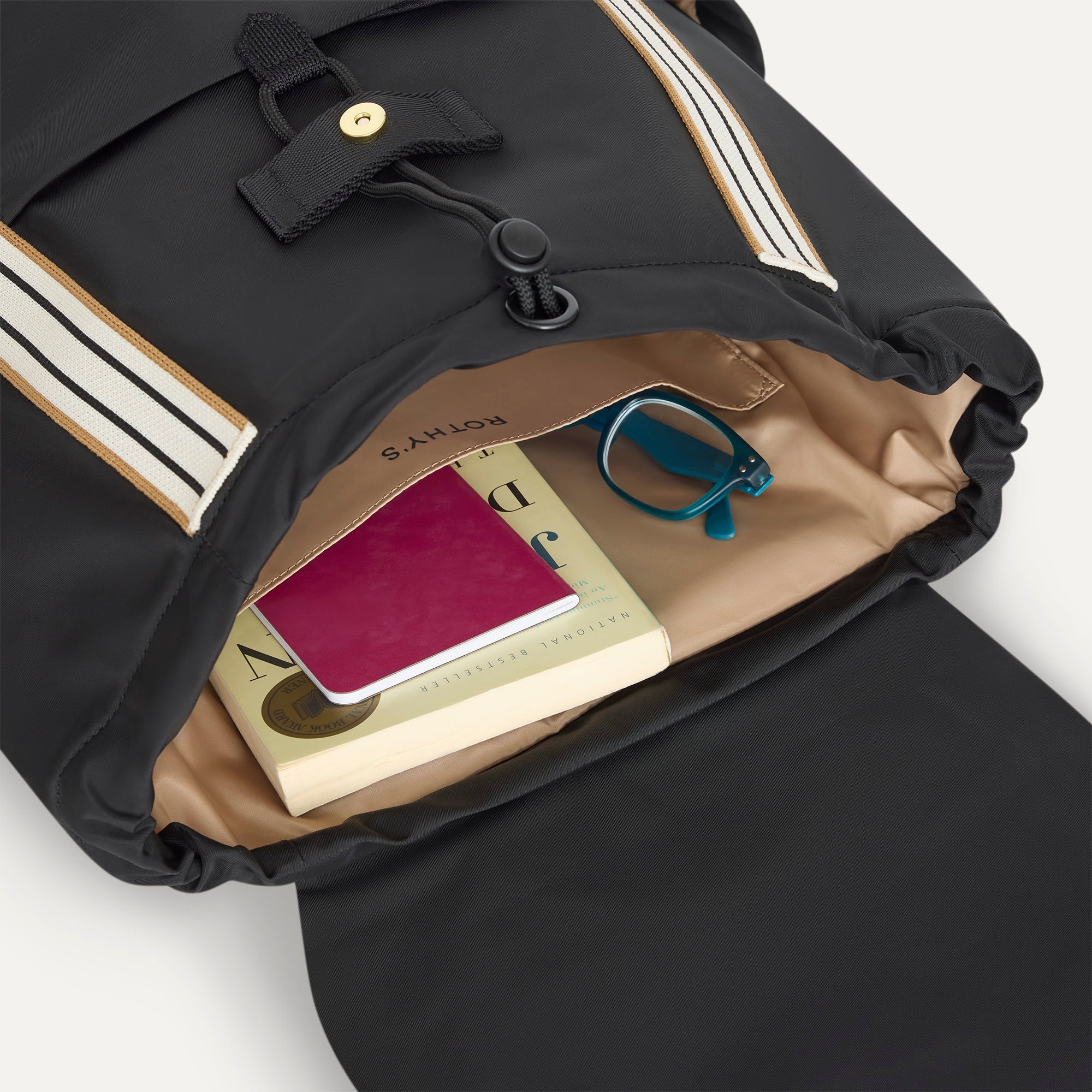 A close up of The Travel Cinch Backpack in Ink showing the interior pockets with a book inside.